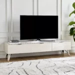 Sade tasarımı ve doğal ahşap dokusuyla öne çıkan Pureline Modern TV Ünitesi, salon ve oturma odalarına ferah ve şık bir görünüm kazandırır. Zamansız çizgileri sayesinde modern, minimalist ve nordik dekorasyon stilleriyle kolayca uyum sağlar. Geniş yüzeyi televizyon yerleşimi için ideal bir alan sunarken, kapaklı yapısı düzenli ve toplu bir görünüm oluşturur. Açık renk tonu mekânı daha aydınlık ve geniş gösterir, yaşam alanlarında dengeli bir atmosfer yaratır. Hem estetik hem de kullanışlı bir çözüm sunan modern TV sehpası, salonunda sade ama güçlü bir stil arayanlar için ideal bir tercihtir. Günlük kullanımda şıklığı ve düzeni bir arada sunar.