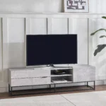 Betonix Loft TV Ünitesi, modern, endüstriyel ve minimal dekorasyon tarzını benimseyenler için özel olarak tasarlanmış güçlü bir TV ünitesi modelidir. Beton görünümlü yüzeyi ve siyah metal ayaklarıyla yaşam alanınıza modern bir karakter kazandırırken, fonksiyonel yapısıyla günlük kullanımda maksimum konfor sunar. Yüksek kaliteli MDF gövde, özel beton dokulu kaplaması sayesinde hem şık bir görünüm sağlar hem de çizilmeye ve aşınmaya karşı dayanıklıdır. Sağlam metal ayaklı TV ünitesi tasarımı, ürüne yüksek taşıma kapasitesi ve uzun ömürlü kullanım avantajı sunar. Yerden yüksek yapısı sayesinde temizlik kolaydır ve mekâna ferahlık katar. Kapaklı dolap bölmeleri ve açık raf alanları ile uydu alıcısı, oyun konsolu, modem, kitap, dergi ve dekoratif objeler için düzenli bir depolama alanı sunar. Bu özellikleri sayesinde salon TV ünitesi, oturma odası TV sehpası, endüstriyel TV dolabı ve modern TV konsolu olarak çok yönlü kullanım sağlar.