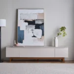 Nordica Minimal TV Ünitesi, modern yaşam alanları için özel olarak tasarlanmış, zamansız çizgilere sahip şık ve fonksiyonel bir TV sehpası / TV ünitesi modelidir. Minimalist tasarımı, doğal ahşap ayakları ve sade renk paletiyle hem modern hem de İskandinav dekorasyon tarzına mükemmel uyum sağlar. Yüksek kaliteli MDF gövde, dayanıklı yüzey kaplaması ve sağlam doğal ahşap ayak yapısı sayesinde uzun yıllar güvenle kullanabilirsiniz. Geniş iç hacmi, kapaklı bölmeleri ve düzenli yapısı ile kablo karmaşasını gizleyen TV ünitesi, salon ve oturma odalarında düzenli bir görünüm sunar. Bu model; televizyon ünitesi, TV sehpası, modern konsol, minimal TV dolabı arayan kullanıcılar için hem estetik hem de kullanışlı bir çözümdür. Düşük ayaklı tasarımı sayesinde duvara yaslı veya tablo ile birlikte dekoratif bir bütünlük oluşturur.